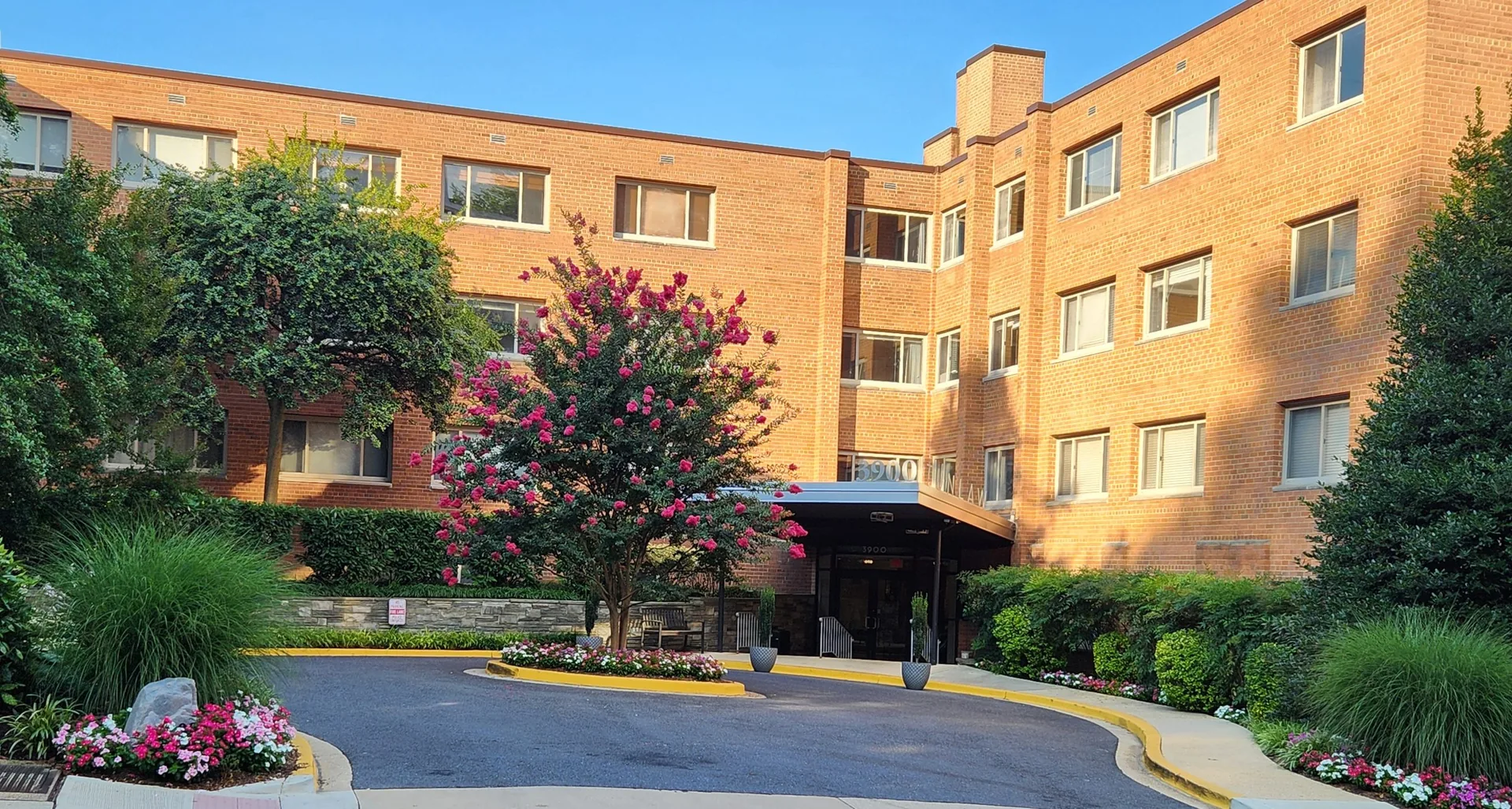 The brick façade and landscaped entrance circle of the 3900 Tunlaw Cooperative on a summer morning